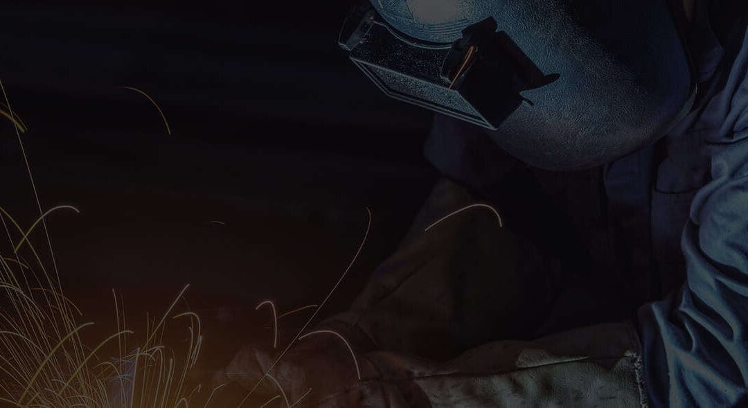 Welder wearing protective gear creating sparks while working with metal.